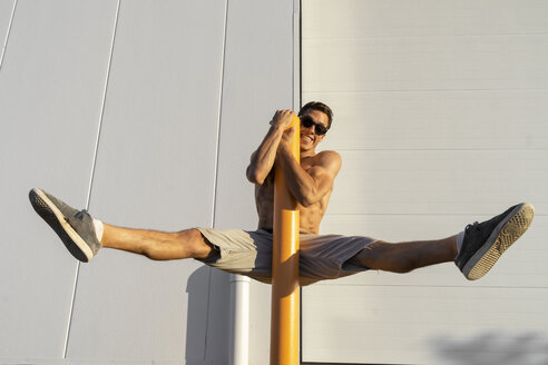 Acrobat straddling on pole, wearing sunglasses - AFVF00973