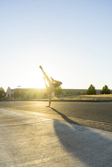 Akrobat übt einarmigen Handstand auf einer Straße bei Sonnenuntergang - AFVF00993