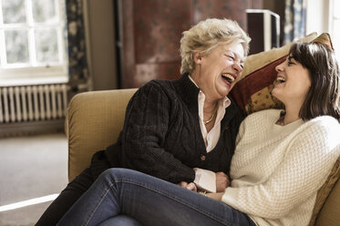 Zwei Frauen, Mutter und Tochter, sitzen Seite an Seite und lachen. - MINF00974