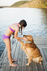 Ein Mädchen im Bikini mit einem Golden Retriever Hund, der seine Pfote hochhebt. - MINF01003