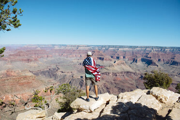 USA, Arizona, Rückenansicht eines in die amerikanische Flagge gehüllten Mannes, der den Blick auf den Grand Canyon National Park genießt - GEMF02169