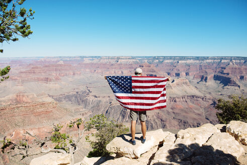 USA, Arizona, Rückenansicht eines Mannes mit amerikanischer Flagge, der den Blick auf den Grand Canyon National Park genießt - GEMF02170