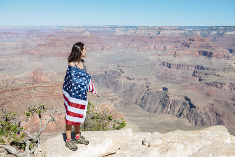 USA, Arizona, Frau in amerikanischer Flagge eingewickelt genießt den Blick auf den Grand Canyon National Park, lizenzfreies Stockfoto