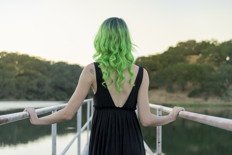 Rückenansicht einer jungen Frau mit grün gefärbtem Haar, die auf einem Steg am See steht, lizenzfreies Stockfoto