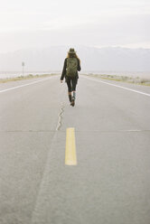 A woman carrying a backpack walking down the centre line of a country road. - MINF01017