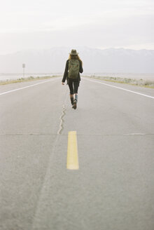 Eine Frau, die einen Rucksack trägt, läuft auf der Mittellinie einer Landstraße. - MINF01017