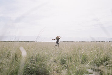 A woman running through long grass, view from a distance. - MINF01019