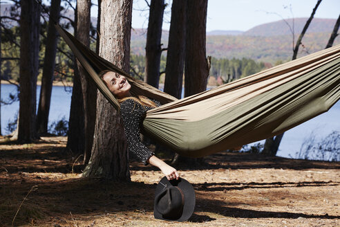 A woman lying in a hammock relaxing, under the pine trees by a lake. - MINF01041