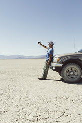 Man leaving against truck in desert, using smart phone, Black Rock Desert, Nevada - MINF01051