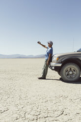 Mann, der gegen einen Lastwagen in der Wüste fährt und ein Smartphone benutzt, Black Rock Desert, Nevada - MINF01051