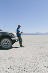 Man leaving against truck in desert, using smart phone, Black Rock Desert, Nevada - MINF01052