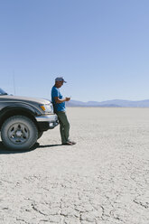 Mann, der gegen einen Lastwagen in der Wüste fährt und ein Smartphone benutzt, Black Rock Desert, Nevada - MINF01052