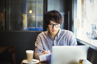 Junger japanischer Mann, der einen Tag in London genießt, in einem Café sitzt und einen Laptop benutzt. - MINF01079