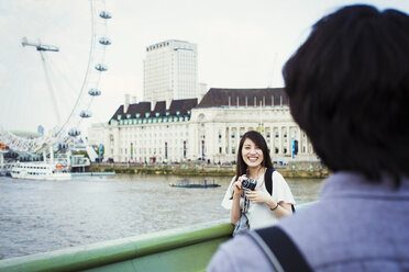 Junger japanischer Mann und Frau genießen einen Tag in London, an der Themse stehend, mit dem London Eye im Hintergrund. - MINF01086