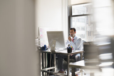 Ein Mann sitzt an einem Schreibtisch in einem Büro und benutzt einen Computer. - MINF01139