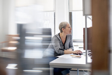 Eine Frau arbeitet in einem Büro an ihrem Schreibtisch und benutzt eine Computermaus. - MINF01140