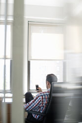 A man seated in a large office chair, leaning back and checking his smart phone. - MINF01142