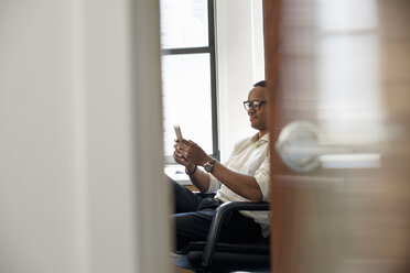 Ein Mann sitzt in einem Büro und schaut auf sein Smartphone. - MINF01148