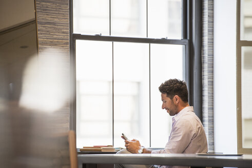 Büroleben: Ein Mann in einem Büro, der sein Smartphone überprüft. - MINF01165