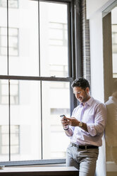 Büroleben: Ein Mann in einem Büro, der sein Smartphone überprüft. - MINF01166