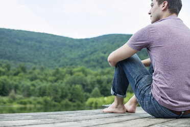 A man sitting on a wooden pier by a lake in summer - MINF01240