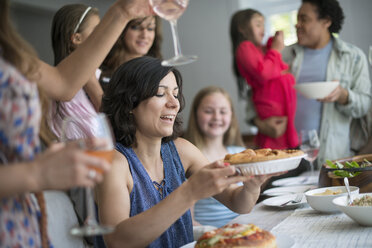 Eine Familie, die sich zum Essen trifft: Erwachsene und Kinder an einem Tisch. - MINF01260