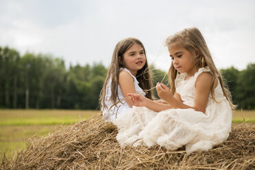 Two girls sitting on top of a haystack playing. - MINF01291