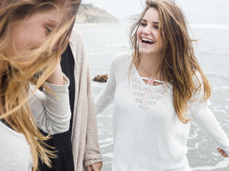 Drei lächelnde junge Frauen, die an einem Strand spazieren gehen. - MINF01336