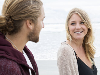 Young man and young woman on a beach, looking at each other, smiling. - MINF01382