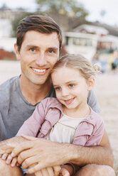 Young girl sitting on her father's lap, looking at camera, smiling. - MINF01392