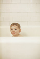 Junge sitzt in einer Badewanne, nimmt ein Bad und lächelt in die Kamera. - MINF01401