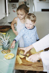 Woman cutting a fresh pineapple for her children. - MINF01406