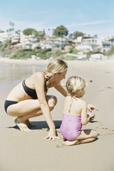 Frau im Bikini spielt mit ihrer Tochter an einem Sandstrand. - MINF01409