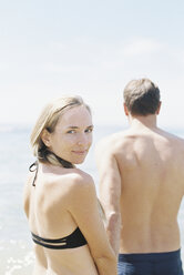 Couple in swimwear by the ocean, woman smiling at camera. - MINF01412