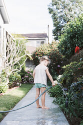 Junges Mädchen steht auf einem Weg im Garten und spielt mit einem Wasserschlauch. - MINF01420
