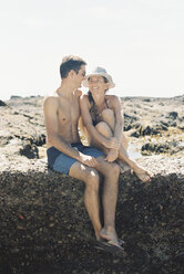 A man and woman, a couple sitting on the beach looking lovingly at each other - MINF01424