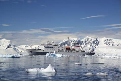 Ein Antarktis-Kreuzfahrtschiff mit aufblasbaren Zodiacs auf den ruhigen Gewässern zwischen Eisschollen und bergiger Landschaft. - MINF01467