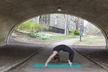 Eine junge Frau im Central Park, in einem schwarzen Trikot und Leggings, macht Yoga. - MINF01476