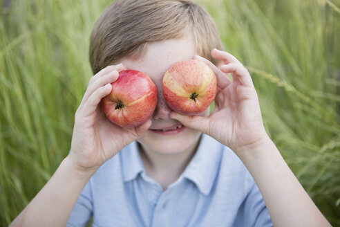 Ein Junge, der zwei rotschalige Äpfel über seine Augen hält. - MINF01497