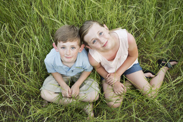 Bruder und Schwester sitzen Seite an Seite im langen Gras. - MINF01506