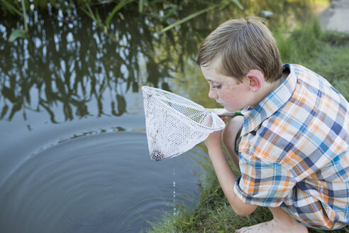 Ein Junge im Freien mit einem Fischernetz, der an einem Flussufer die Gegenstände im Netz untersucht. - MINF01526
