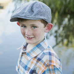 Ein Junge in einem karierten Hemd und einer Stoffmütze mit breiter Krempe steht an einem Flussufer. - MINF01527