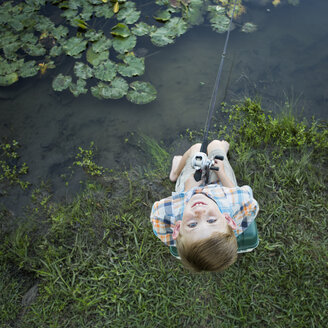 A young boy outdoors, standing on a riverbank looking up above his head. - MINF01528