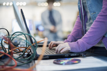 Eine Person, die einen Laptop-Computer benutzt. Scheibe und Kabel auf dem Tresen. Reparaturwerkstatt. - MINF01575
