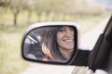 Frau in einem Auto, die ihr Spiegelbild im Seitenspiegel anlächelt. - MINF01620