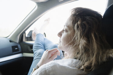 Frau in einem Auto auf einer Autoreise, ihre Beine und nackten Füße aus dem Fenster. - MINF01621