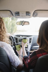 Zwei Frauen in einem Auto mit Kaffeetassen in der Hand, Blick über die Schulter. - MINF01622