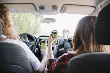 Two women in a car on a road trip, bare feet on the dashboard. View from behind. - MINF01623