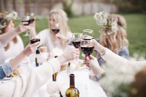 Eine Gruppe von Freundinnen sitzt an einem Tisch und stößt mit Rotwein an. - MINF01653