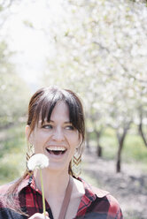 Eine Frau, die eine Pusteblumenuhr in der Hand hält und lacht. - MINF01693